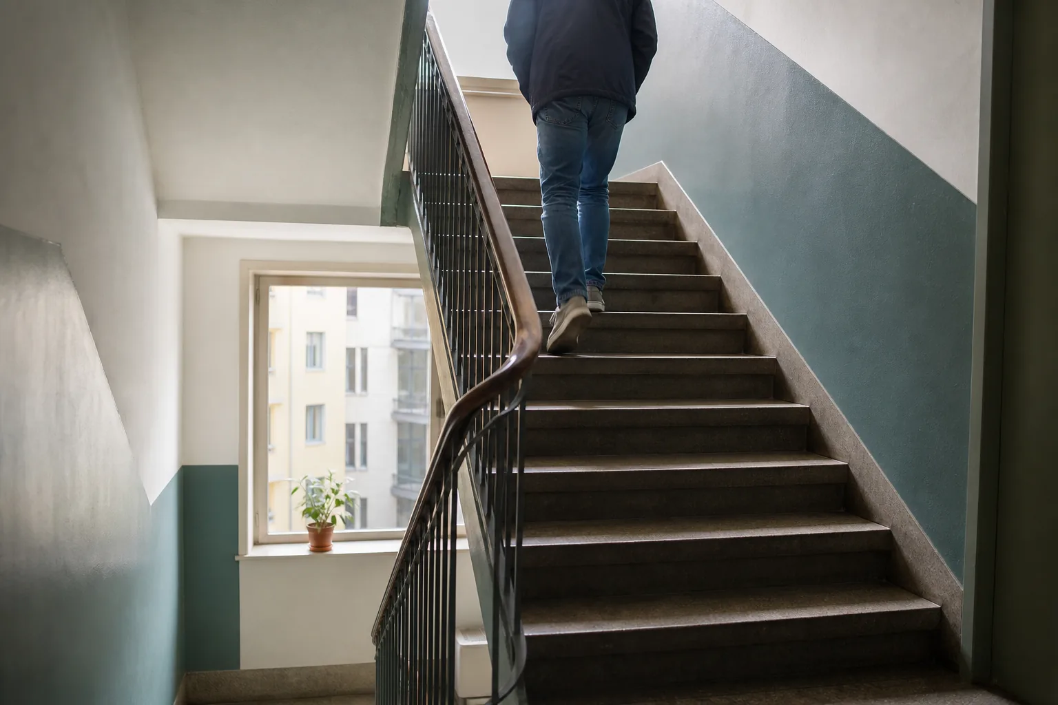 En anonym person går uppför en trappa i ett svenskt flerbostadshus med dagsljus från ett fönster.