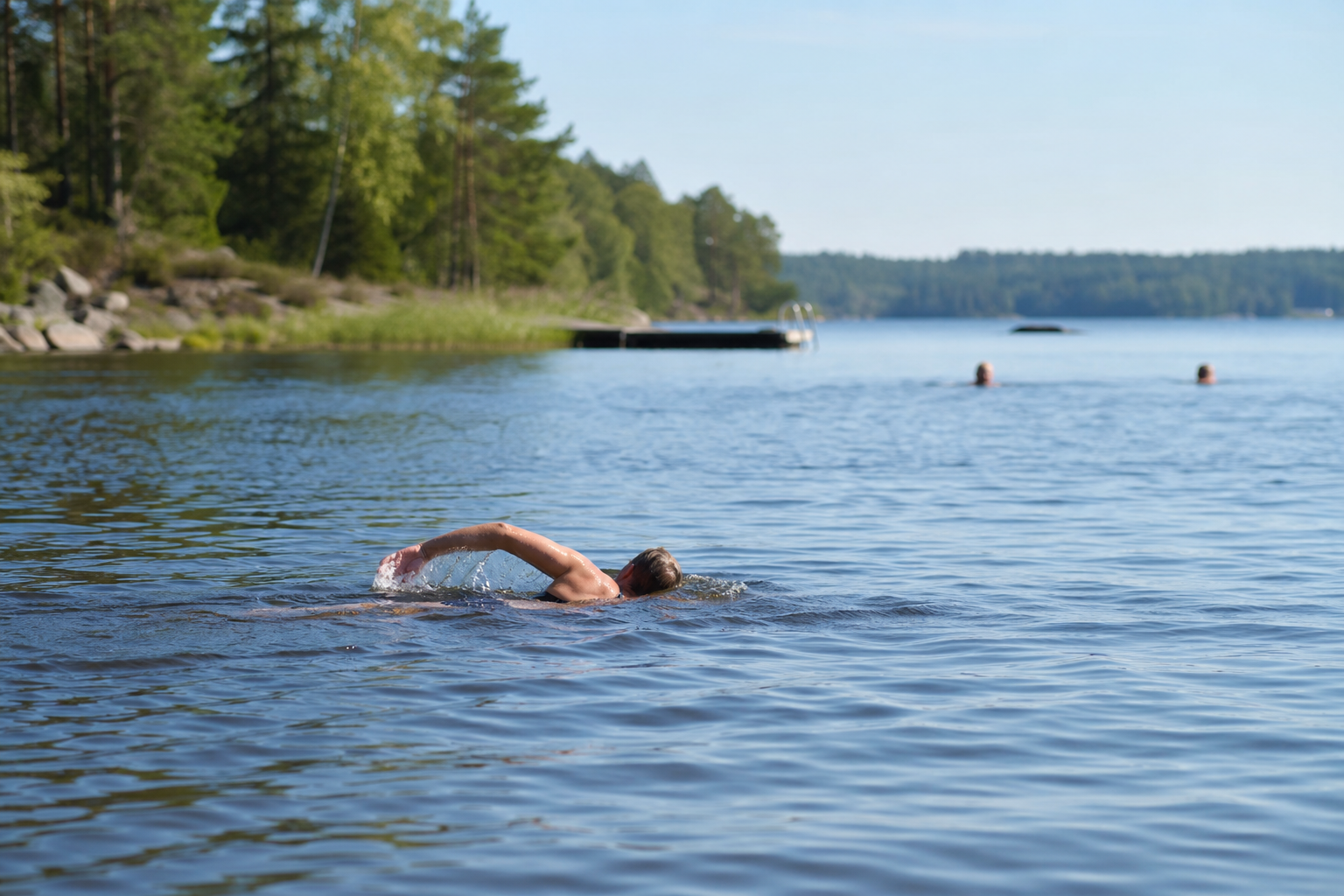 Person som simmar lugna frisimtag i en sjö medan andra badande syns oskarpt längre bort.